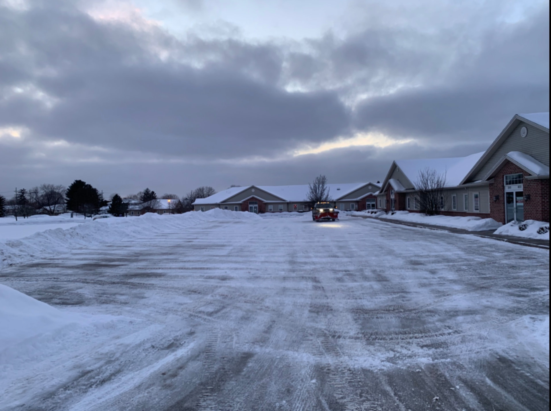 Plow truck clearing a large senior living community parking lot at dawn