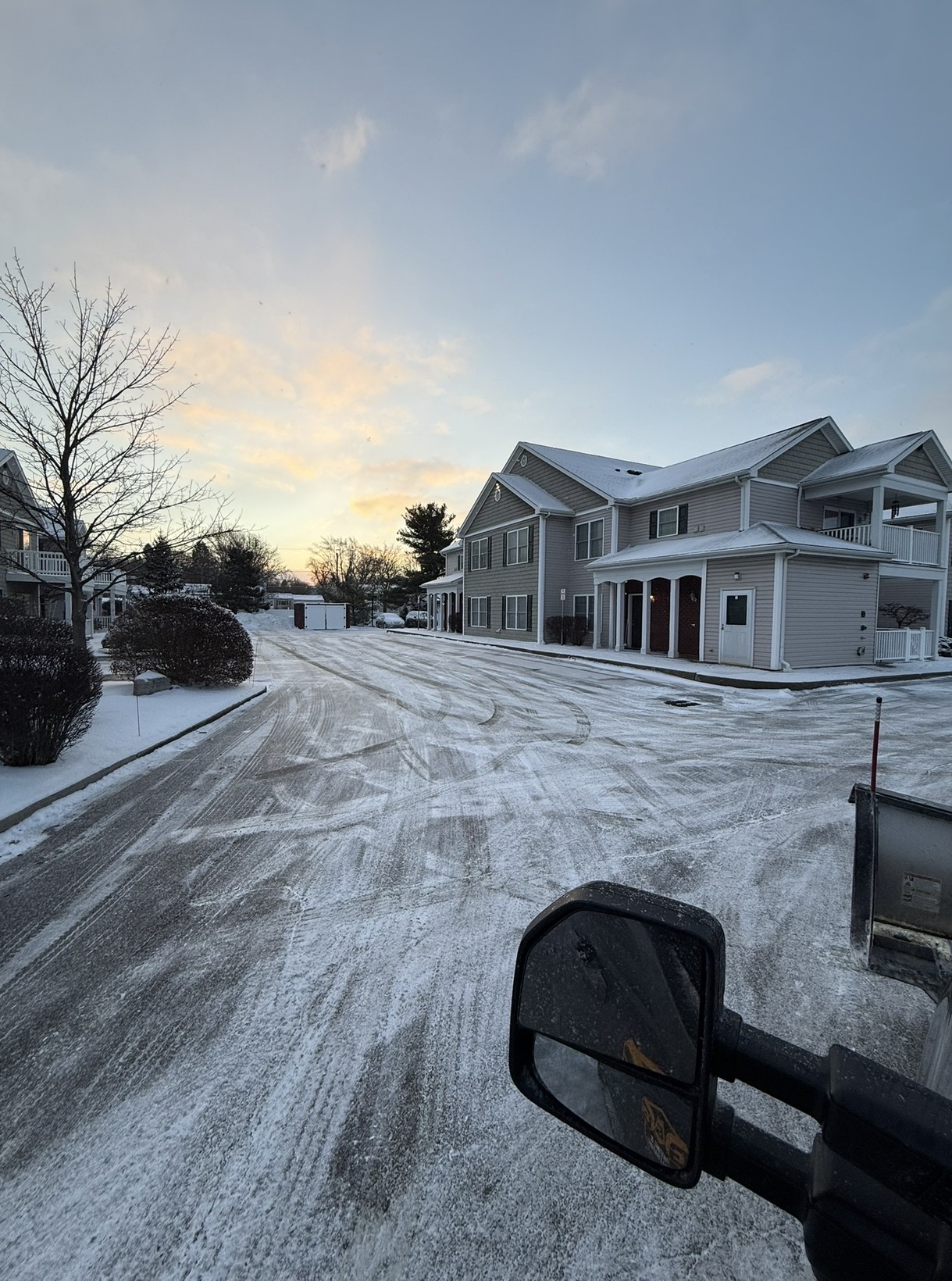 Plow truck clearing a snow-covered residential drive at sunrise