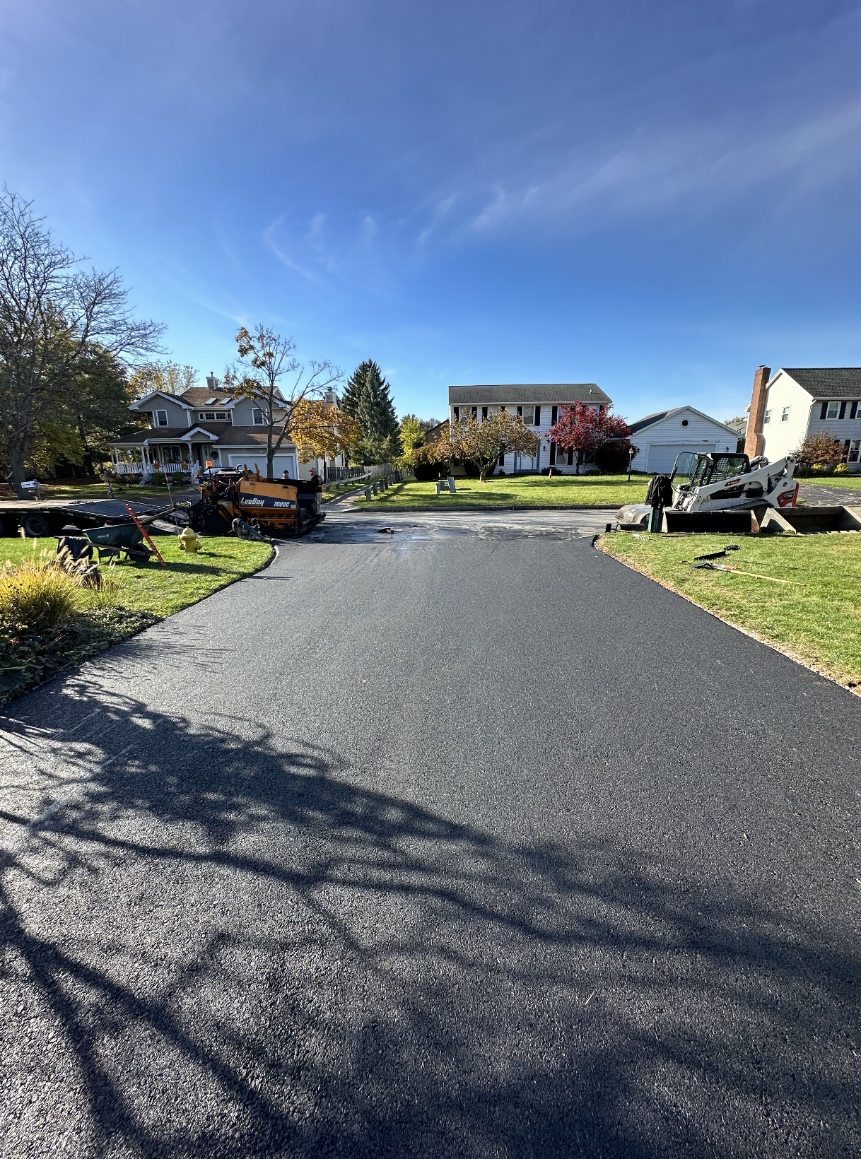 Newly paved residential driveway with paver and skid steer on site