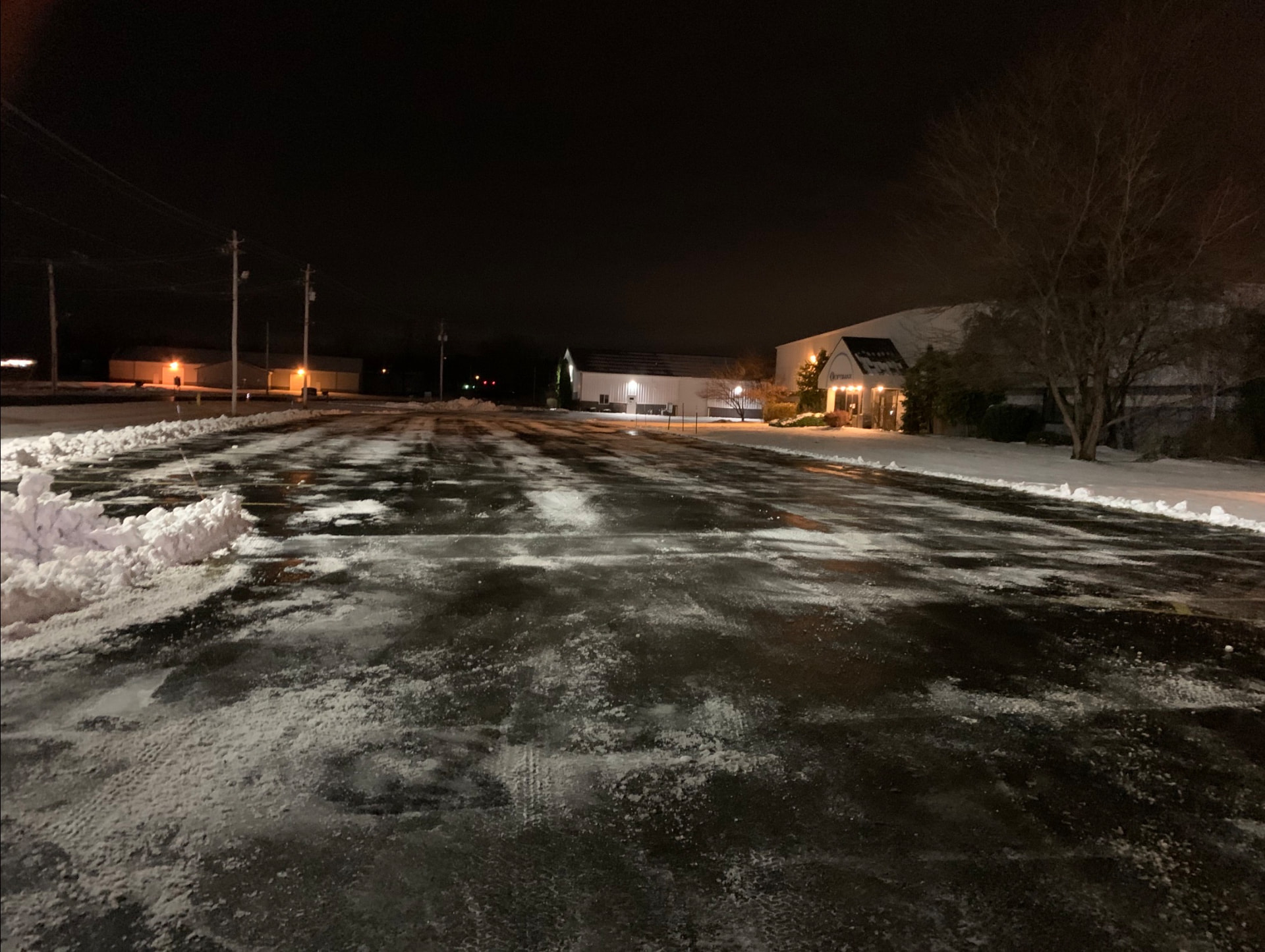Commercial parking lot plowed clean at night with snow banks piled to the side